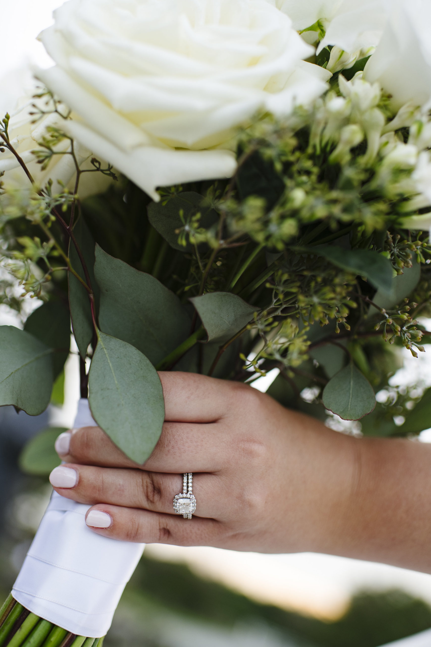 White roses and greenery bouquet with white ribbon tie and exposed stems. Beautiful halo ring photo with engagement ring. - Pearl Weddings &amp; Event