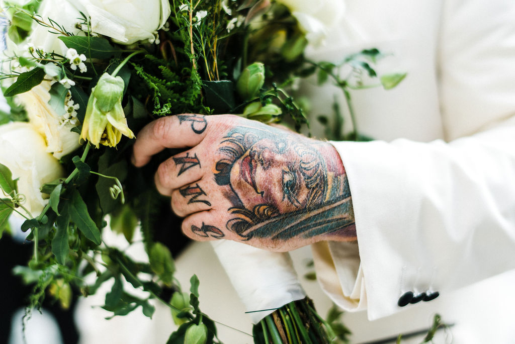 Grooms tattooed hand holding his wife bouquet filled with passion flowers - Pearl Weddings &amp; Events