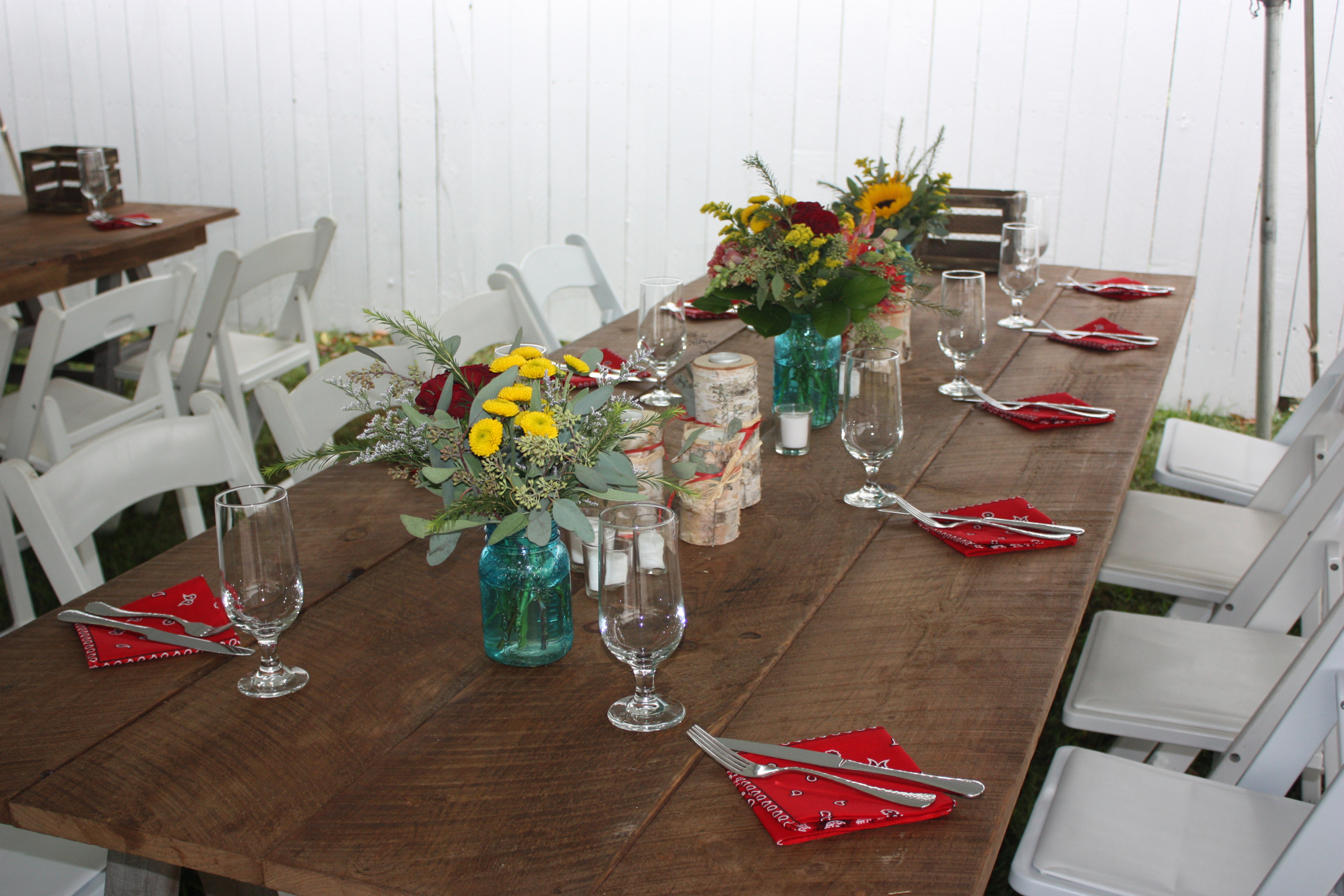 Red napkins, farm tables, white garden chairs and blue mason jars with sunflowers for this rustic backyard wedding - Pearl Weddings &amp; Events