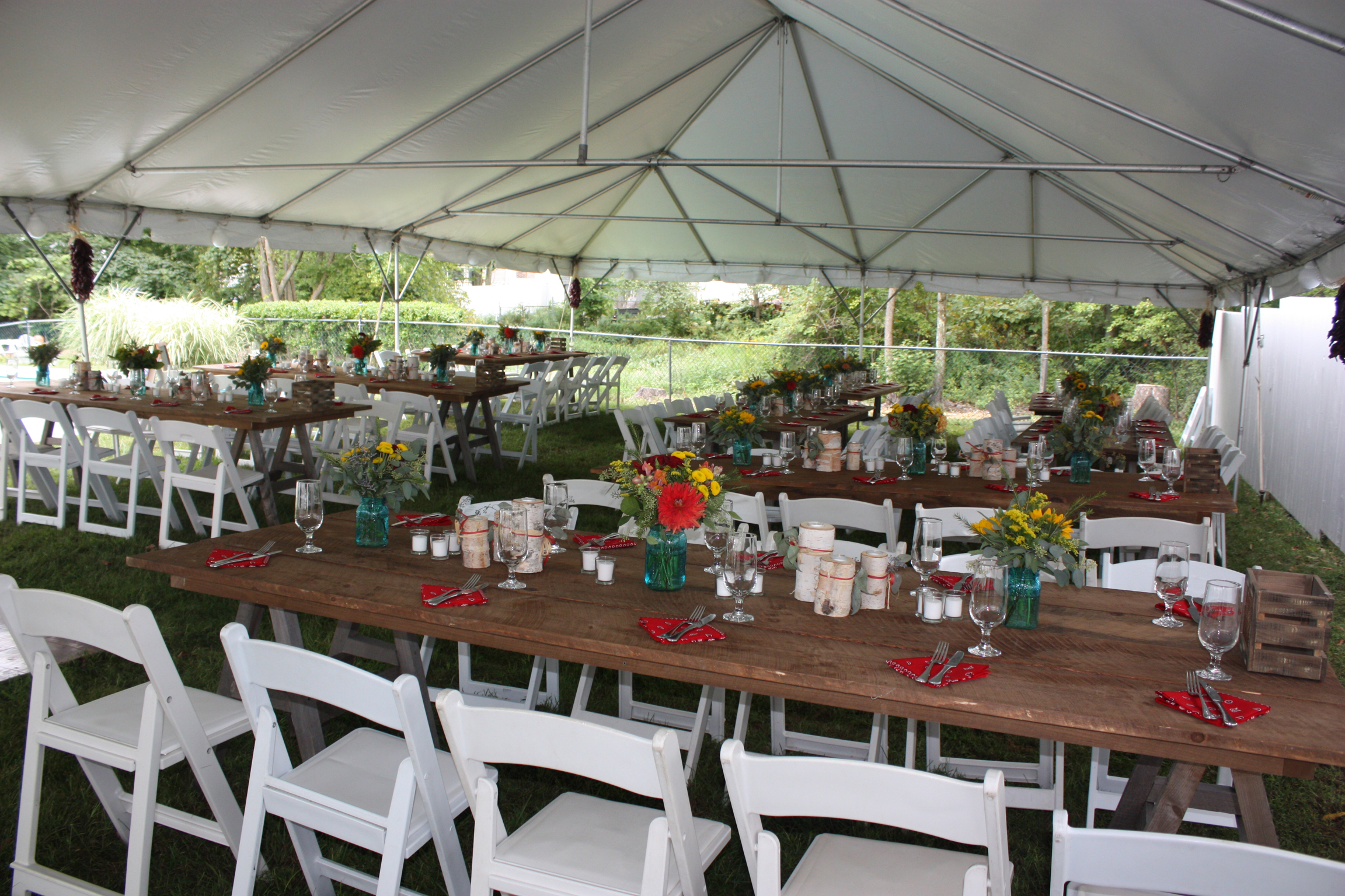 Red napkins, farm tables, white garden chairs and blue mason jars with sunflowers for this rustic backyard wedding - Pearl Weddings &amp; Events