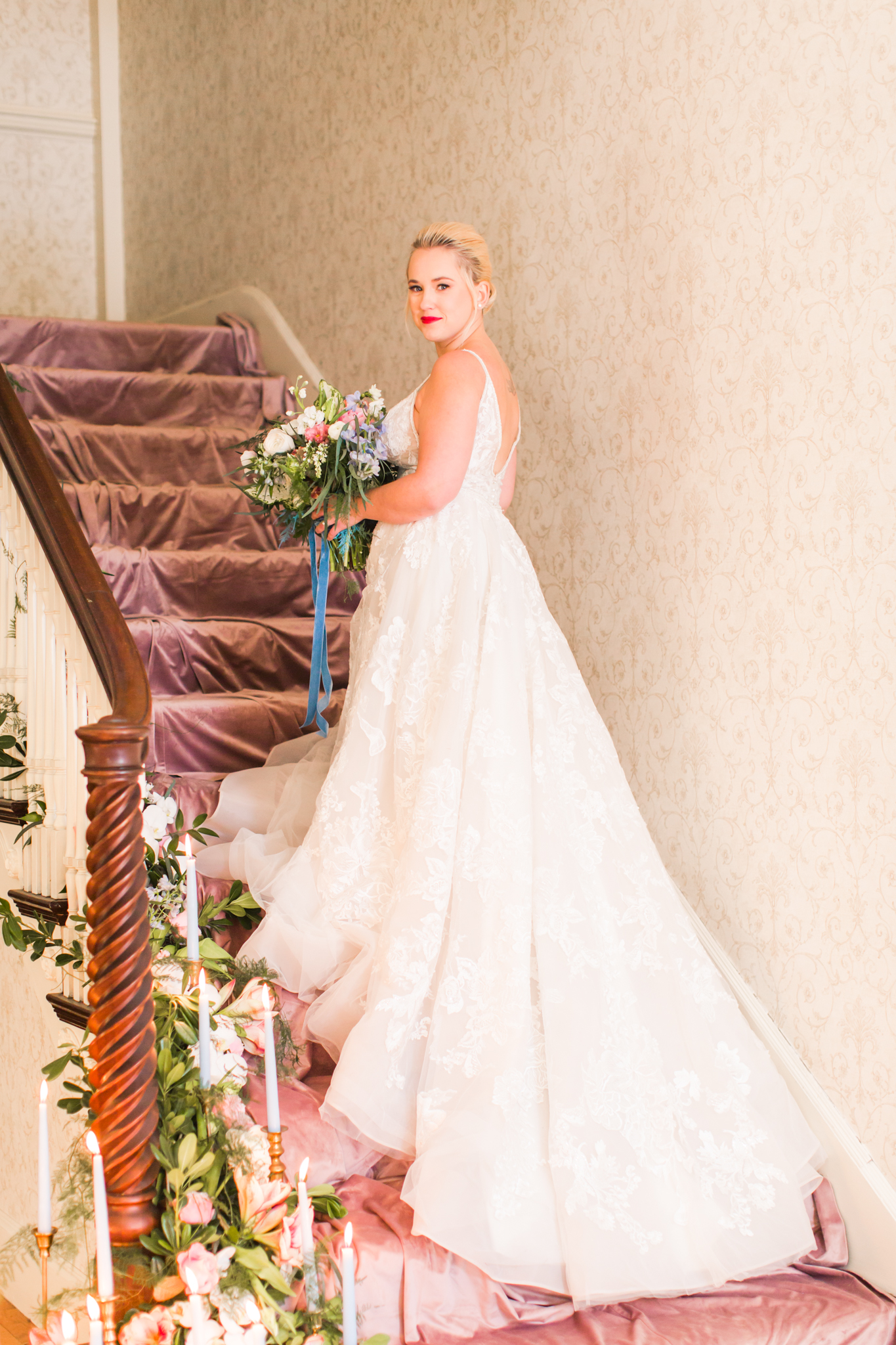 Bride posed on the staircase with pink velvet stairs and florals cascading down with light blue candles - Pearl Weddings &amp; Events