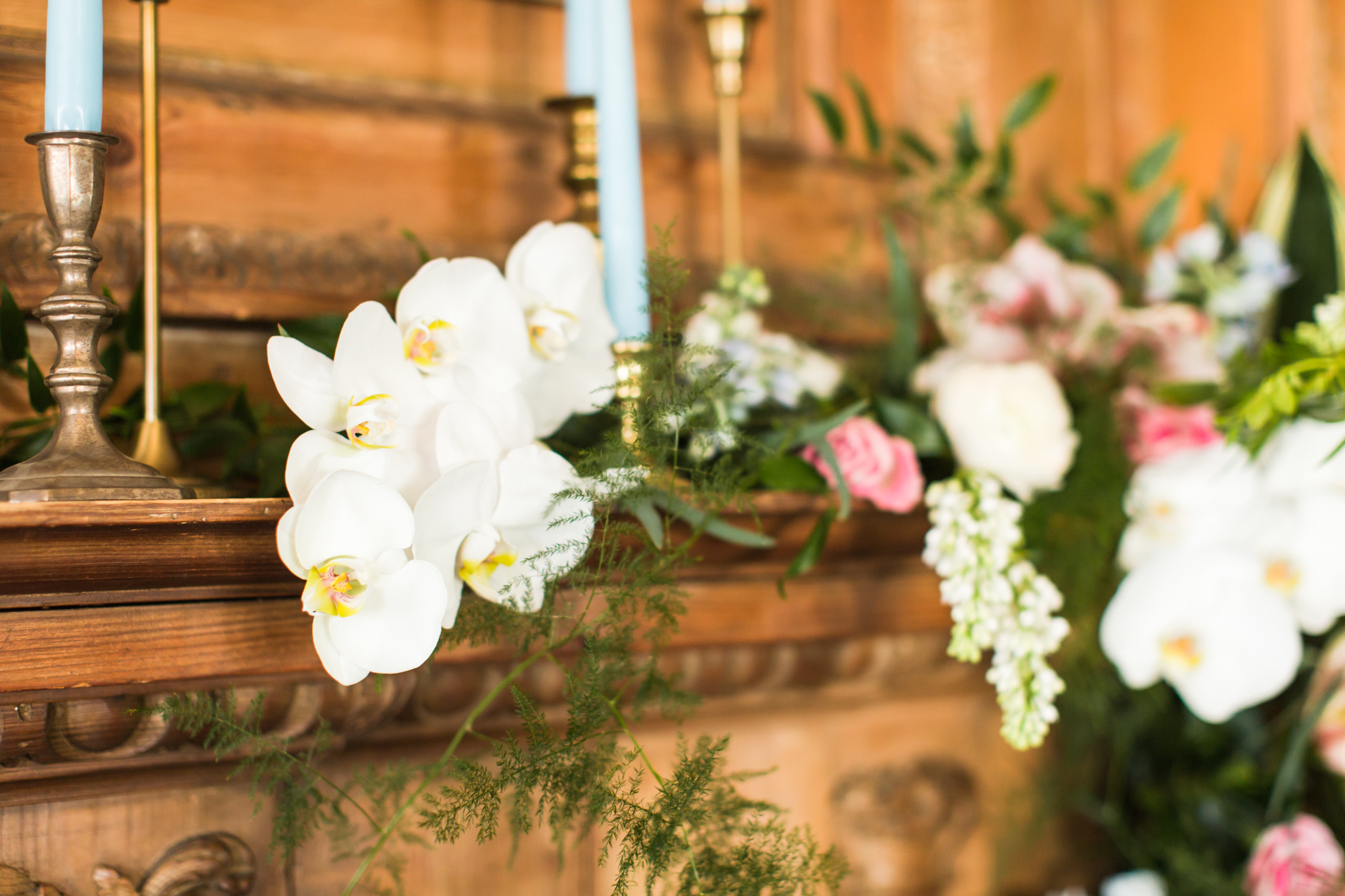 White orchids, greenery, pink and coral florals with light blue candles and gold candle holders on a wooden fire place - Pearl Weddings &amp; Events
