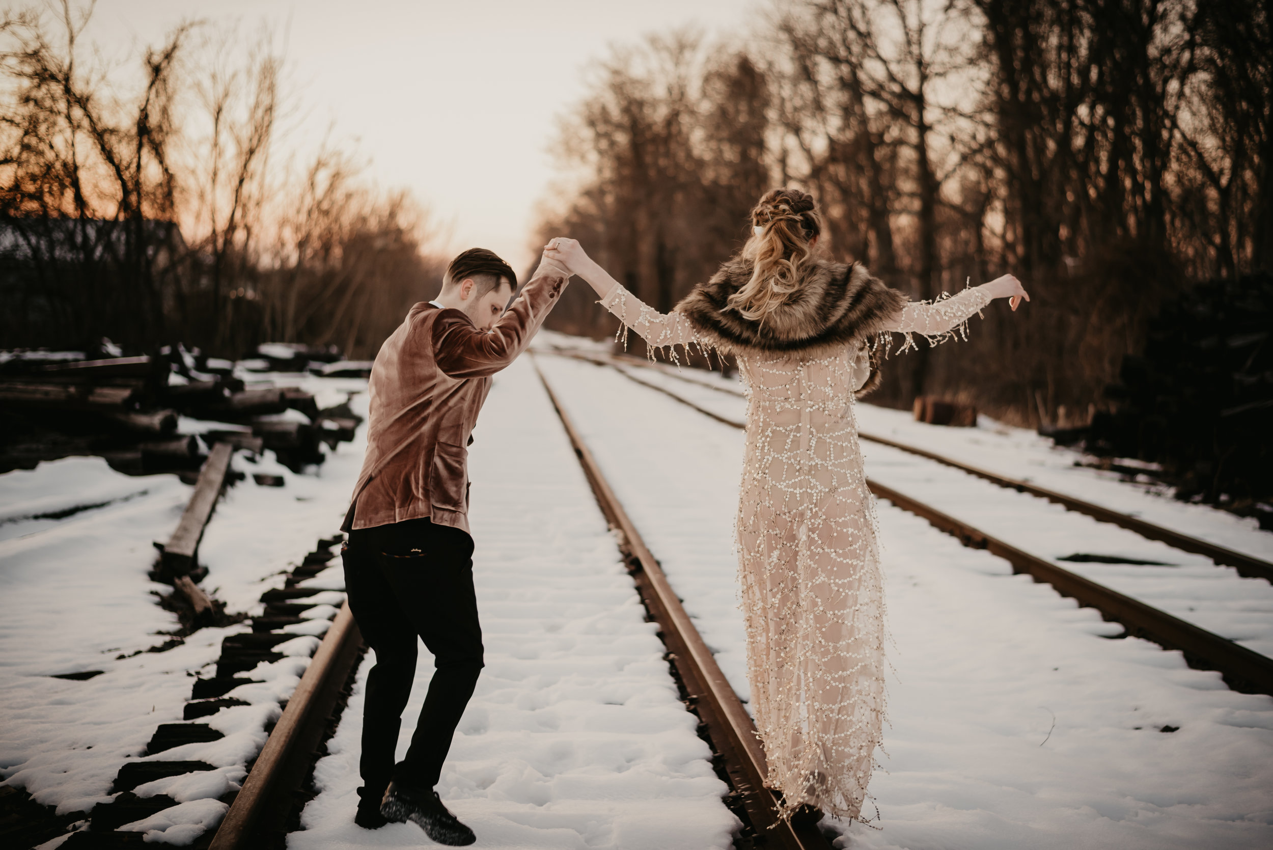Groom in a velvet jacket, bride in a sequins dress with a shawl on her wedding day walking the train rails in the middle of winter! - Pearl Weddings &amp; Events