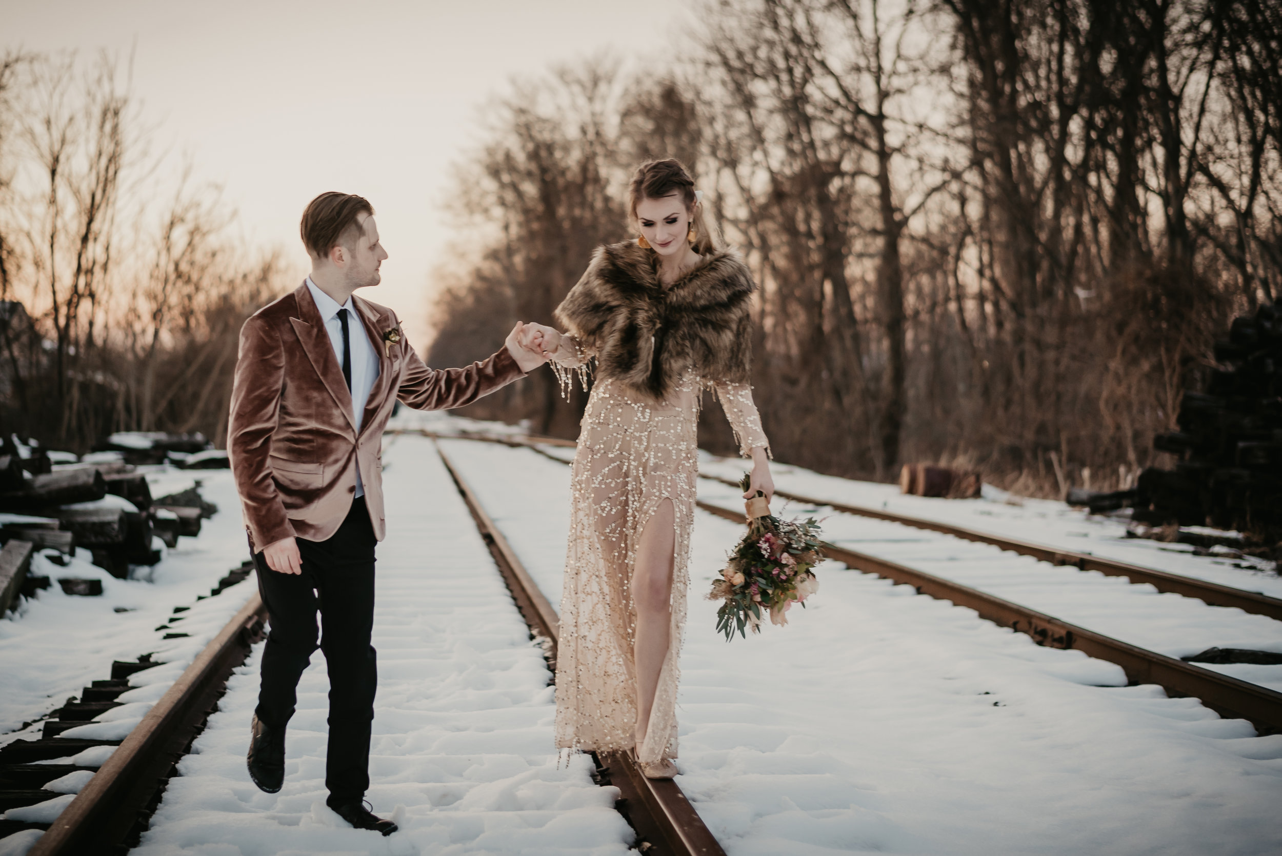 Groom in a velvet jacket, bride in a sequins dress with a shawl on her wedding day walking the train rails in the middle of winter! - Pearl Weddings &amp; Events