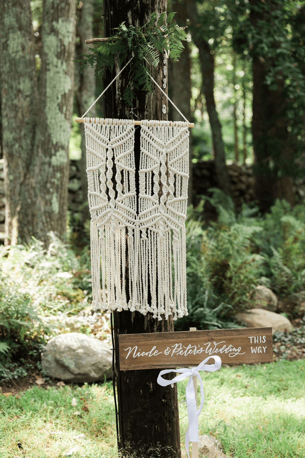 A woven tapestry hanging in the woods and a sign leading to the wedding