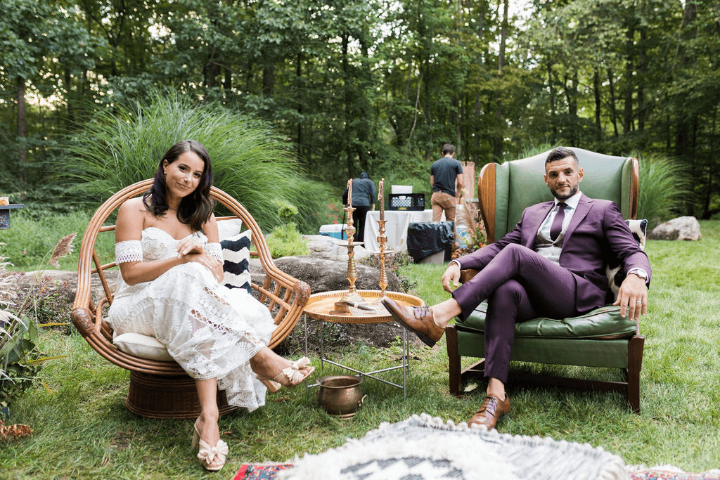 Bride and groom sit together in giant cozy chairs from their wedding lounge
