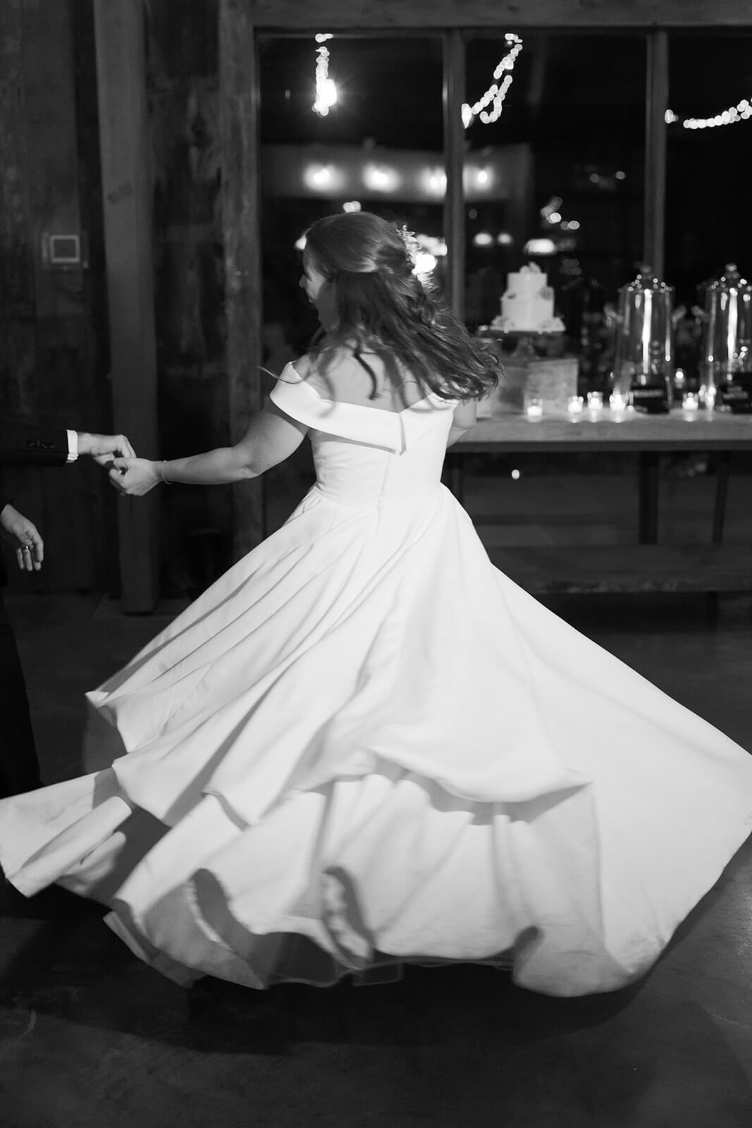 A black and white photo of the bride twirling her dress as she dances