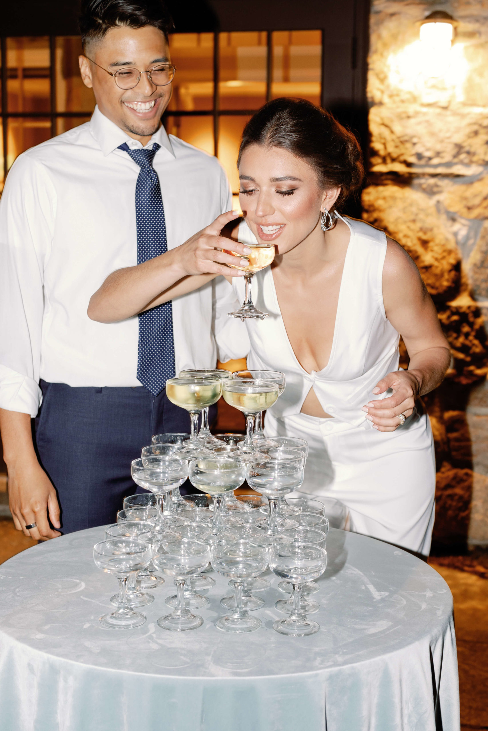 bride sips from champagne tower as groom smiles during their New England Wedding