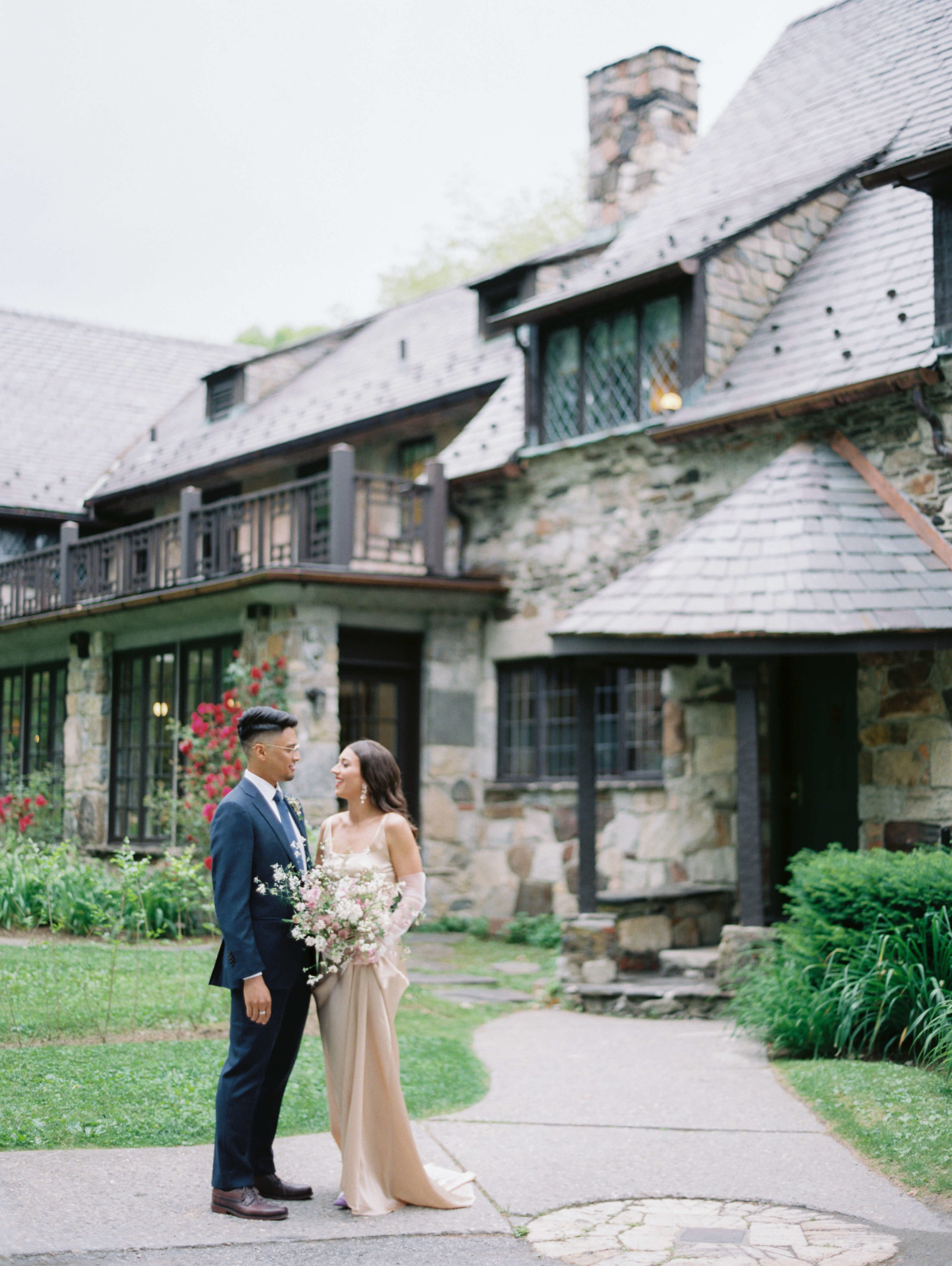 bride and groom stand in front of a stone building