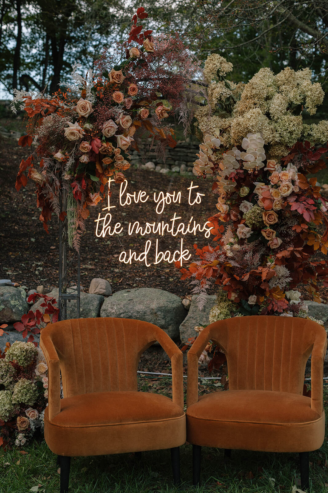 Two velvet chairs with a neon sign and floral arch in the background at fall tented wedding 