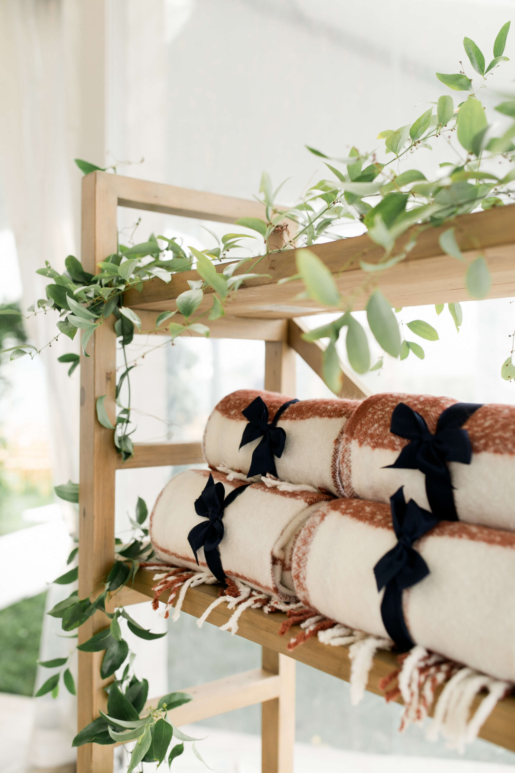 Warm blankets for wedding guests placed on wooden shelf decorated with greenery 