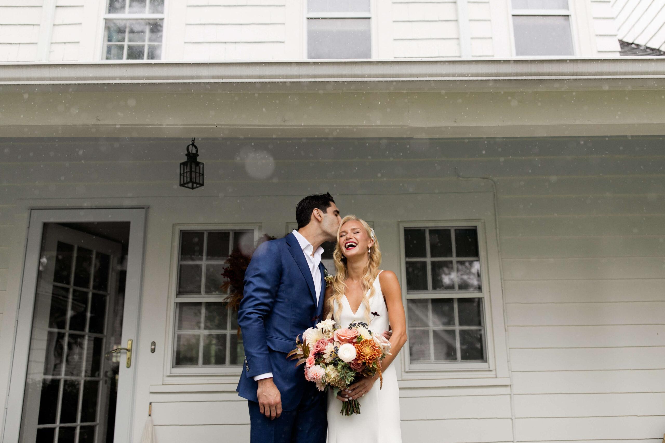 Bride and groom in front of house during their rainy wedding day.