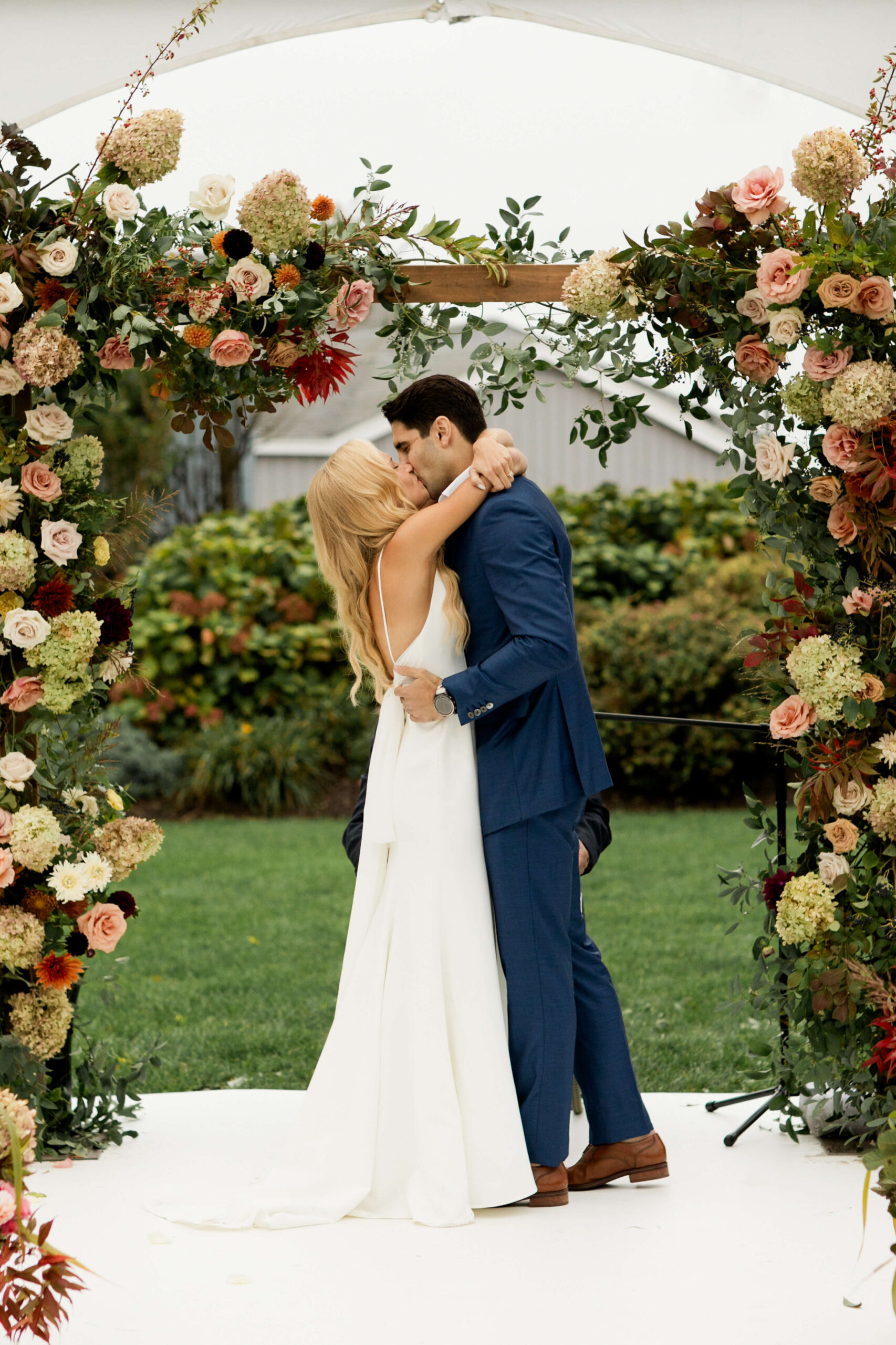 Bride and groom kissing underneath floral arch